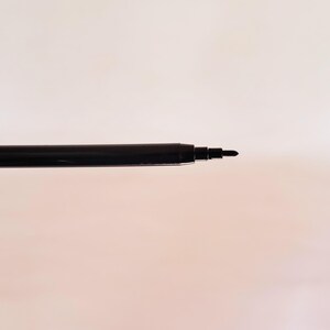 May include: A black pen tip extending from a cylindrical black barrel. The writing instrument features a smooth, dark finish with a tapered point designed for precision. The structure is simple, showing the exposed nib and the main body casing.