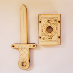 sword through finger magic trick. A plywood laser cut device.  Wooden hand held box decorated as the King of hearts playing card. A finger is pushed through a hole in the box.  A small wooden sword is then pushed into the box and out the other side