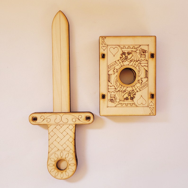 sword through finger magic trick. A plywood laser cut device.  Wooden hand held box decorated as the King of hearts playing card. A finger is pushed through a hole in the box.  A small wooden sword is then pushed into the box and out the other side