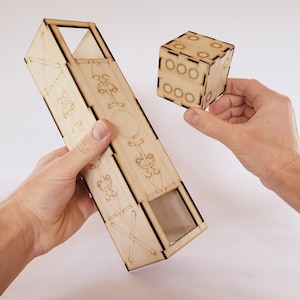 May include: A wooden box with a cutout window and a wooden dice with holes on each side. The box has a decorative design on the front and sides.