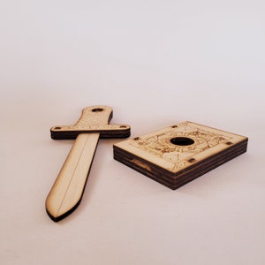 sword through finger magic trick. A plywood laser cut device.  Wooden hand held box decorated as the King of hearts playing card. A finger is pushed through a hole in the box.  A small wooden sword is then pushed into the box and out the other side