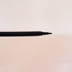 May include: A black pen tip extending from a cylindrical black barrel. The writing instrument features a smooth, dark finish with a tapered point designed for precision. The structure is simple, showing the exposed nib and the main body casing.