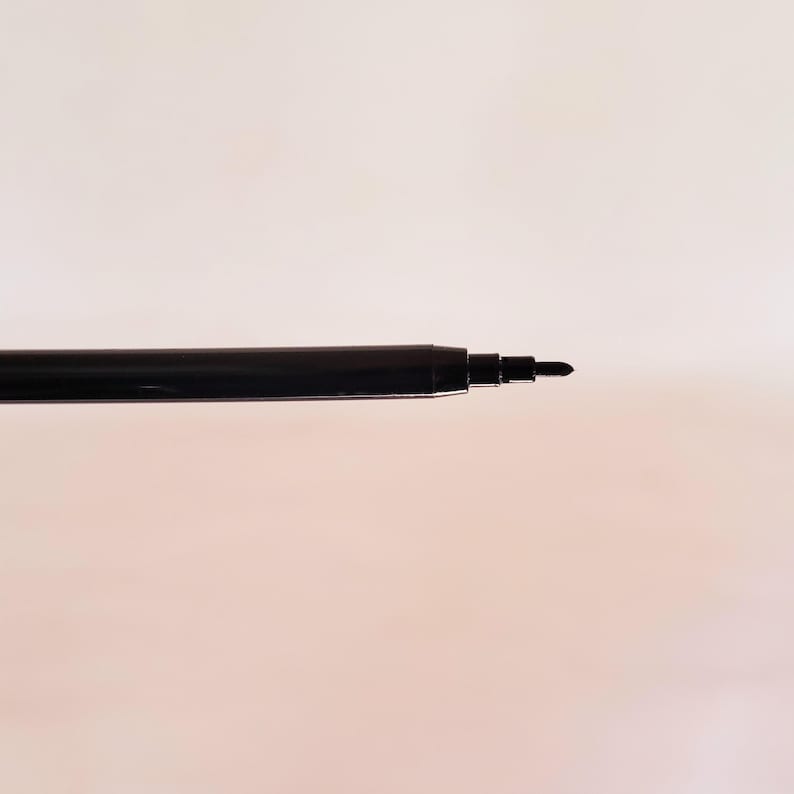 May include: A black pen tip extending from a cylindrical black barrel. The writing instrument features a smooth, dark finish with a tapered point designed for precision. The structure is simple, showing the exposed nib and the main body casing.