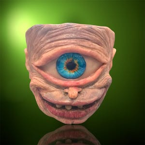 May include: A unique, sculpted face with a single, large eye. The eye is a vibrant blue with a detailed iris. The face has a wrinkled, textured appearance, with a smiling mouth and visible teeth. The background is a gradient of green.