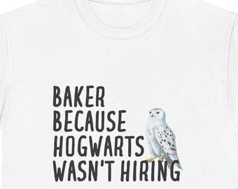 May include: White t-shirt with the text "BAKER BECAUSE HOGWARTS WASN'T HIRING" in black, accompanied by a watercolor illustration of a snowy owl. The shirt is a casual wear item.