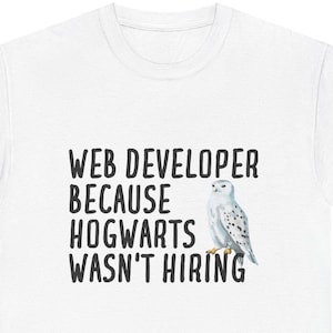 Può includere: T-shirt bianca con la scritta "WEB DEVELOPER BECAUSE HOGWARTS WASN'T HIRING" in nero. Un'illustrazione ad acquerello di un gufo bianco è a destra del testo. La t-shirt è un capo casual.