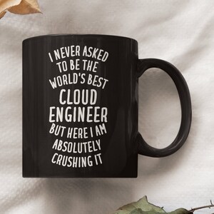 Peut inclure: Mug à café noir avec du texte blanc qui dit "Je n'ai jamais demandé à être le meilleur ingénieur cloud du monde, mais voilà, je suis en train de tout écraser".