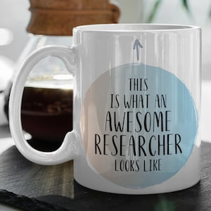 May include: White ceramic coffee mug with a blue and peach watercolor circle design. The text "This is what an awesome researcher looks like" is printed in black on the mug.