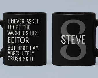 Może przedstawiać: Dwa czarne kubki do kawy. Jeden kubek ma napis "I never asked to be the world's best editor but here I am absolutely crushing it". Drugi kubek ma literę "S" z nazwą "STEVE" poniżej.