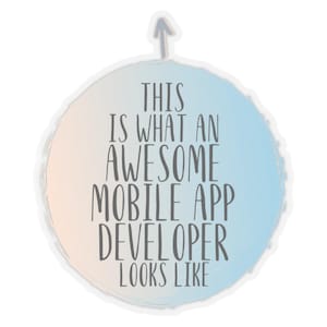 May include: A round sticker with a light blue and peach gradient background and the text "THIS IS WHAT AN AWESOME MOBILE APP DEVELOPER LOOKS LIKE" in grey letters. An upward-pointing arrow is at the top.