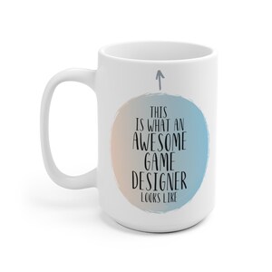May include: White ceramic coffee mug with a blue and orange circle graphic that says "This is what an awesome game designer looks like".