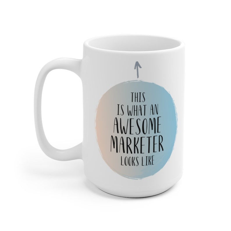 May include: White ceramic coffee mug with a blue and orange watercolor circle design. The text "This is what an awesome marketer looks like" is printed in black on the circle.
