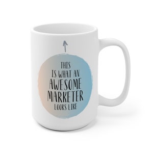 May include: White ceramic coffee mug with a blue and orange watercolor circle design. The text "This is what an awesome marketer looks like" is printed in black on the circle.