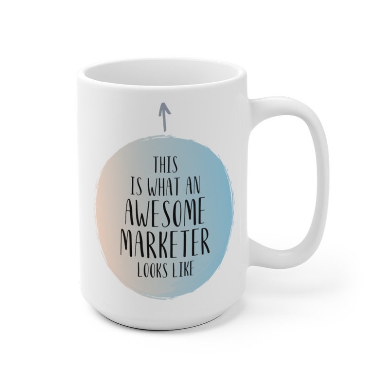 May include: White ceramic coffee mug with a blue and orange watercolor circle design. The text "This is what an awesome marketer looks like" is printed in black on the circle.