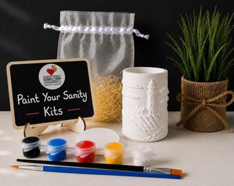 May include: A craft kit featuring a white ceramic lighthouse cylinder, a small chalkboard sign with the text "Paint Your Sanity Kits", a sheer white drawstring bag with yellow filler, five small paint pots, and two paintbrushes.