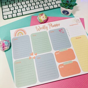 May include: A weekly planner featuring a rainbow design and hearts. The planner has sections for each day of the week, Monday to Sunday, with space for notes and important tasks.
