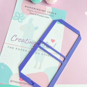 May include: Purple plastic ruler with a frame shape for creating post-it note frames. The ruler has the text "BOOKBINDING TOOLS" and "Reglas de Encuadernacion" on it. The text "Post it Frame ruler" is also on the ruler.