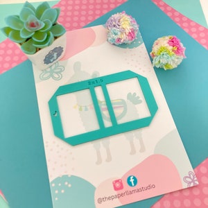 May include: A turquoise blue stencil with a 2x1.5 inch grid pattern. The stencil is on a white background with pink and blue polka dots.