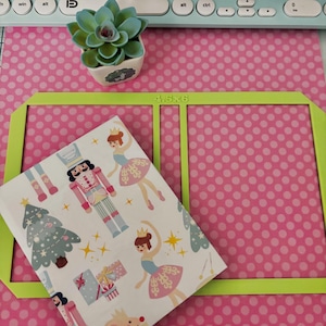 May include: A green cutting mat with a pink polka dot background. A white notebook with a Christmas themed design is placed on the mat. The notebook has a design of a nutcracker, a ballerina, a Christmas tree, and presents. The text "4.5x6" is printed on the mat.