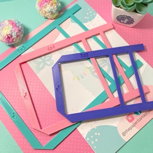 May include: Four plastic frames in different sizes, 3x3, 4x4, 5x5, and 7x7 inches, for creating pom poms. The frames are in pink, blue, and turquoise colors. The frames are on a pink and white polka dot background.