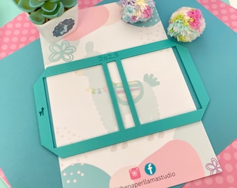 Puede incluir: Plantilla de plástico turquesa con un rectángulo recortado de 7,6 x 6,3 cm. La plantilla está diseñada para manualidades y presenta una ilustración de llama. La plantilla está sobre un fondo rosa y azul con lunares blancos.