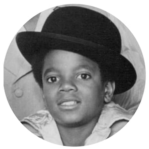May include: A young boy wearing a black bowler hat and a white shirt. He is looking at the camera and smiling.