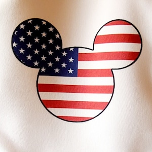 May include: A white fabric with a red, white, and blue American flag design in the shape of Mickey Mouse's head.
