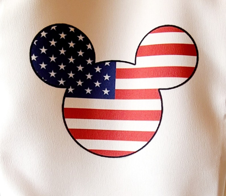 May include: A white fabric with a red, white, and blue American flag design in the shape of Mickey Mouse's head.