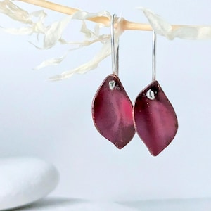 May include: A pair of dangle earrings with a deep burgundy red petal shape. The earrings are made of metal and have a silver hook.