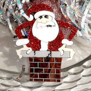 May include: A red and white glitter Santa Claus figurine stuck in a brick chimney. The Santa Claus has a grumpy expression and is holding onto the chimney with both hands.