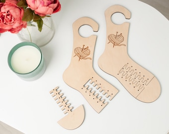 Könnte beinhalten: Zwei hölzerne Sockenstrickvorrichtungen mit einem Garnball- und Stricknadel-Design. Die Vorrichtungen sind aus hellbraunem Holz gefertigt und haben Löcher für Stricknadeln. Es gibt auch ein separates Holzstück mit Löchern für Stricknadeln.