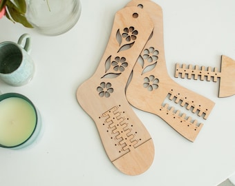 Könnte beinhalten: Holzsockenstrickmaschine mit Blumendesigns und einem Lineal zum Messen der Socken Größe. Die Maschine ist aus hellem braunem Holz gefertigt und hat eine natürliche Oberfläche.