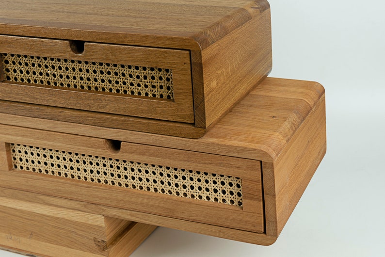 May include: Two stacked wooden storage boxes with rounded edges and a natural brown finish. Each box features a single drawer with a front panel made of woven light beige cane webbing and a small semi-circular cutout for opening the drawer.