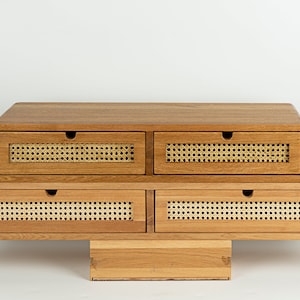 May include: A wooden desk organizer featuring four drawers with rounded edges and light-colored woven cane panels on the front. Each drawer has a small circular cutout for opening. The unit is constructed from light brown wood with a visible grain.