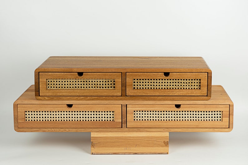 May include: A wooden desk organizer featuring four drawers with rounded edges and light-colored woven cane panels on the front. Each drawer has a small circular cutout for opening. The unit is constructed from light brown wood with a visible grain.