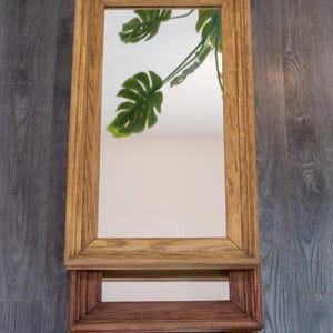 May include: A wooden mirror with a shelf underneath. The mirror has a light brown frame and the shelf is a darker brown.
