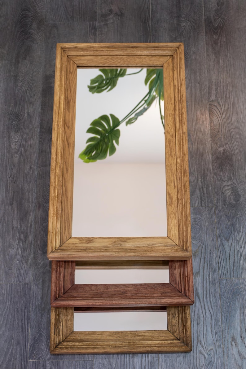 May include: A wooden mirror with a shelf underneath. The mirror has a light brown frame and the shelf is a darker brown.