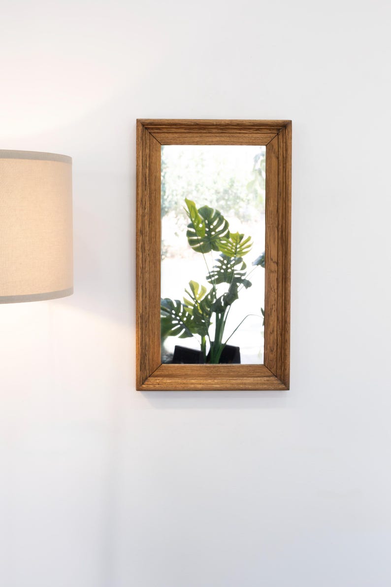 May include: A rectangular wooden framed mirror with a reflection of a green leafy plant in a pot.
