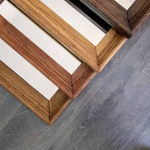 May include: Four wooden picture frames with different wood stains, stacked on top of each other. The frames are all rectangular and have a simple design.