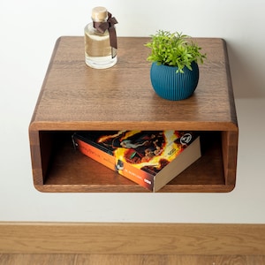 May include: A dark wood floating shelf with a book, a small plant in a blue pot, and a clear glass bottle with a brown ribbon.