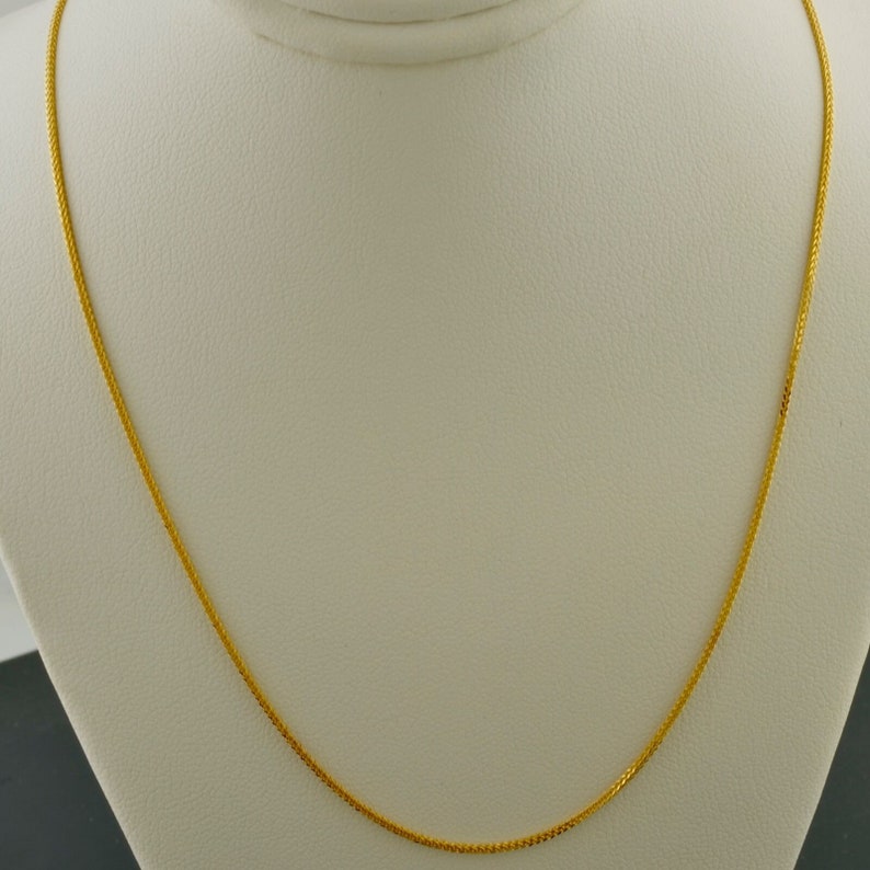 May include: A gold chain necklace on a white display stand.