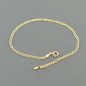 May include: A gold chain bracelet with a delicate, figaro link design. The bracelet is made of 14k gold and has a lobster clasp closure.