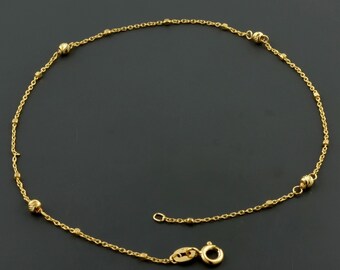 May include: A gold anklet with a delicate chain and small round beads. The anklet has a lobster clasp closure.
