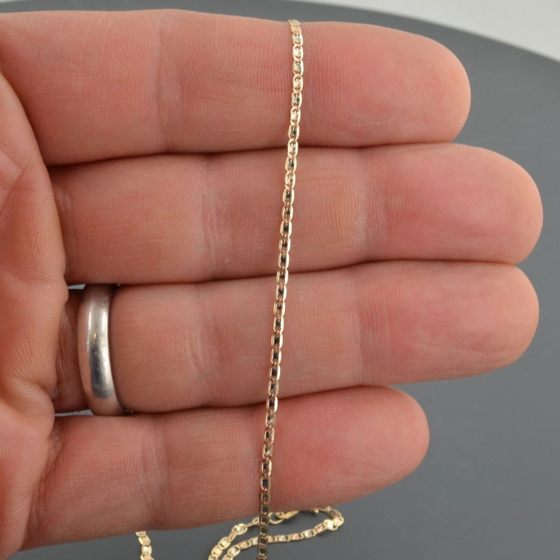 May include: A gold chain necklace with a box chain design. The chain is about 18 inches long and is shown on a hand.