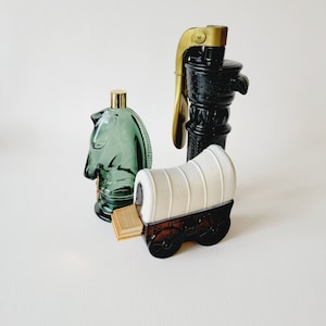May include: Three vintage glass cologne bottles shaped like a horse, a wagon, and a water pump. The horse and wagon are green and white, and the water pump is black with gold accents.