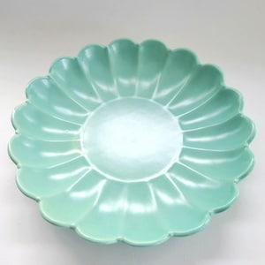 May include: A light green ceramic serving bowl with a scalloped edge. The bowl has a circular center and a petal-like design around the rim. The bowl is a soft, pastel green color.