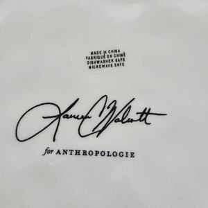 May include: White ceramic dish with black text and signature. The text includes "Made in China", "Dishwasher Safe", "Microwave Safe", and "for ANTHROPOLOGIE". The signature is in black cursive.