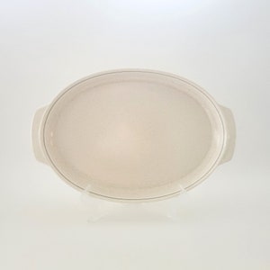 May include: A white oval ceramic serving dish with a black rim and two handles. The dish has a speckled texture.