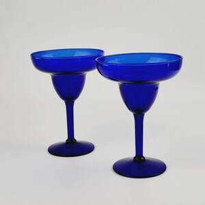 May include: Two cobalt blue glass margarita glasses with a wide bowl and a tall stem.