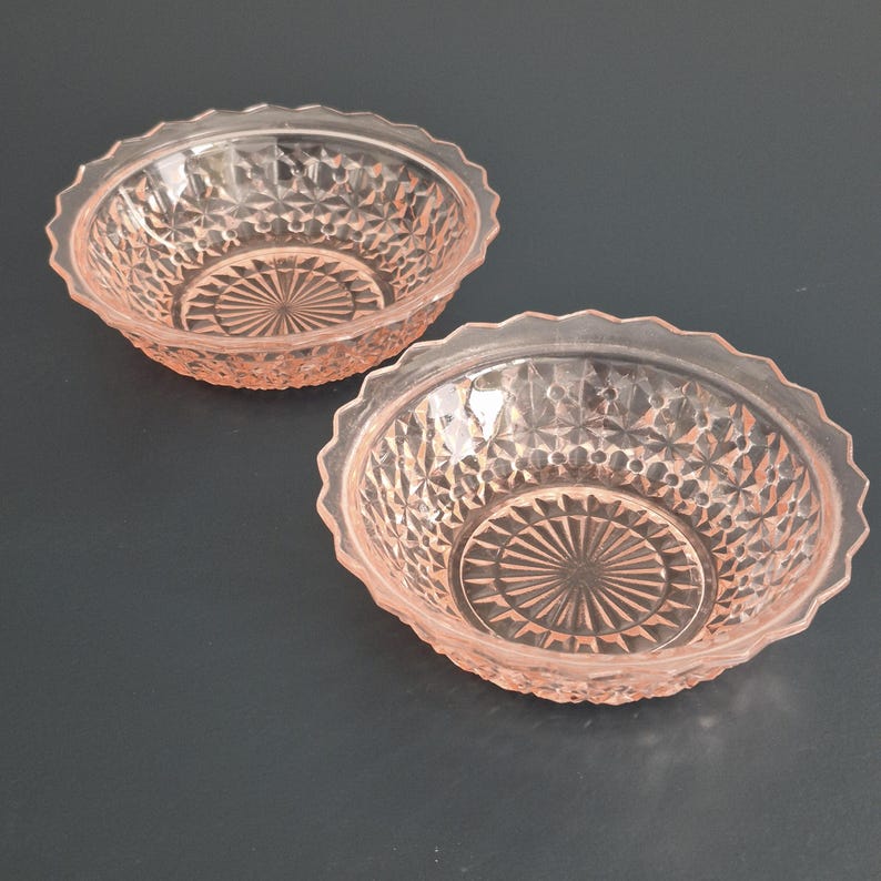 K&ouml;nnte beinhalten: Zwei rosa Glasschalen mit einem strukturierten Rautenmuster und gewellten R&auml;ndern. Die Schalen haben ein kreisf&ouml;rmiges Design in der Mitte. Die Schalen sind wahrscheinlich zum Servieren von Speisen oder zum Ausstellen von Dekorationsartikeln gedacht.